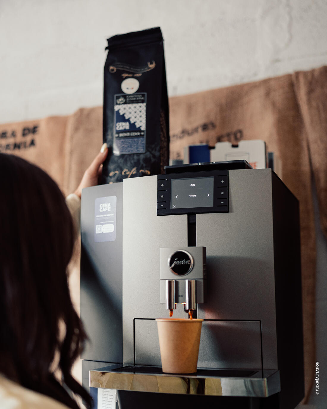 Le Blend Cena Café, café en grains torréfié par les Comptoirs Jeanne d'Arc, présenté au-dessus d'une Jura en pleine extraction