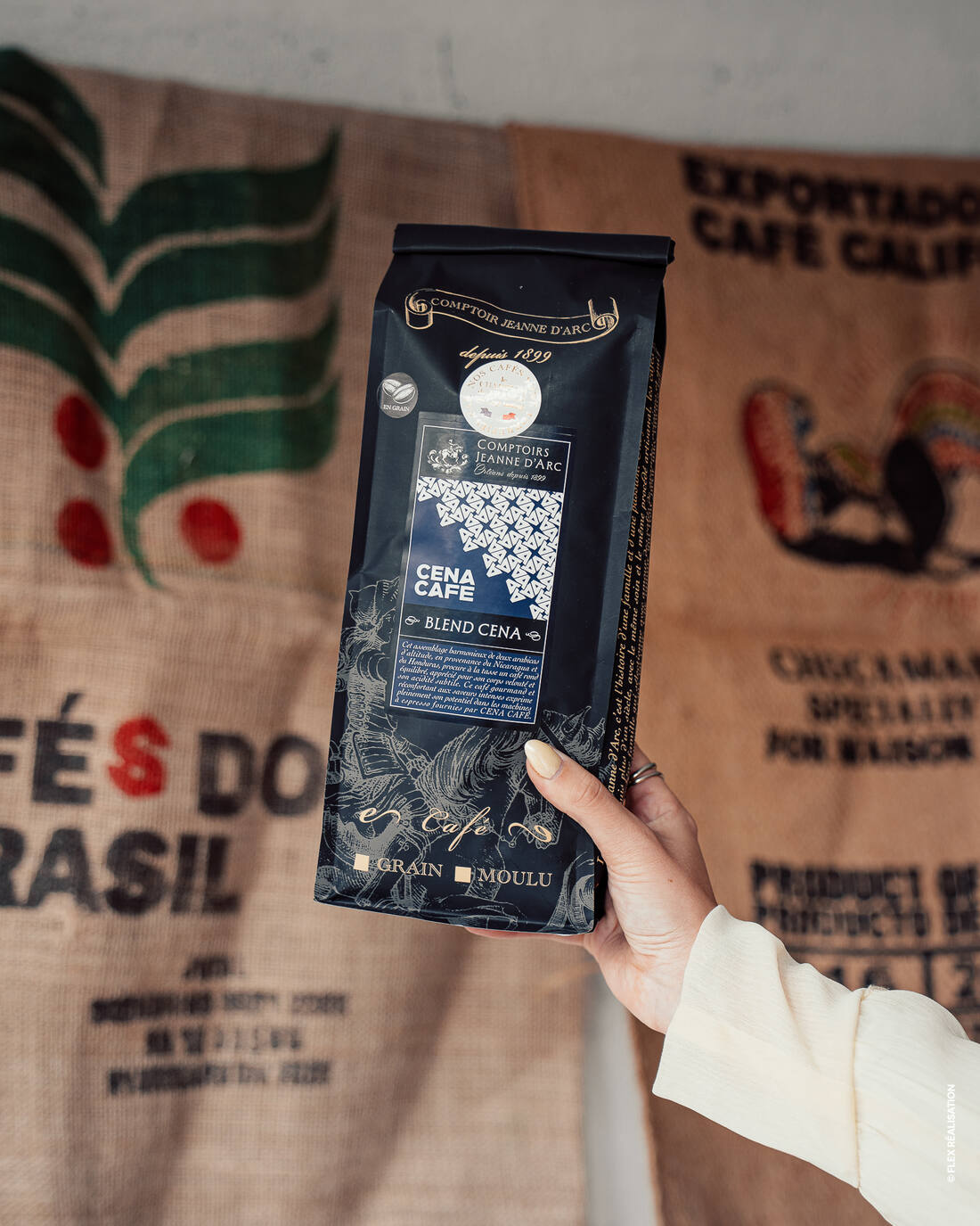 Sachet Blend Cena Café en grains devant les toiles de jute des origines de café exposées au showroom